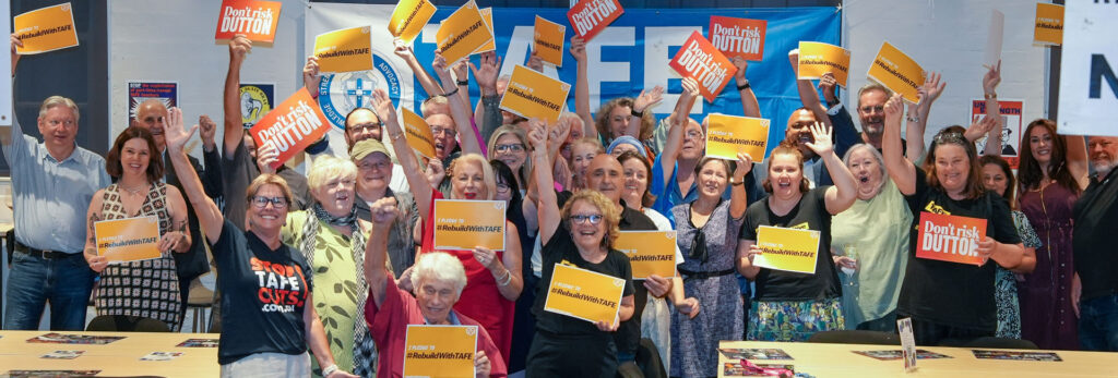 General Secretary Maxine Sharkey, Vice President Sharryn Usher and dozens of TAFE teachers raise their arms and banners celebrating victory in a campaign to rebuild TAFE