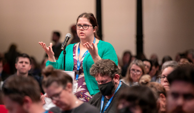 Standing woman speaks into the microphone during the New South Wales Teachers Federation Annual Conference.