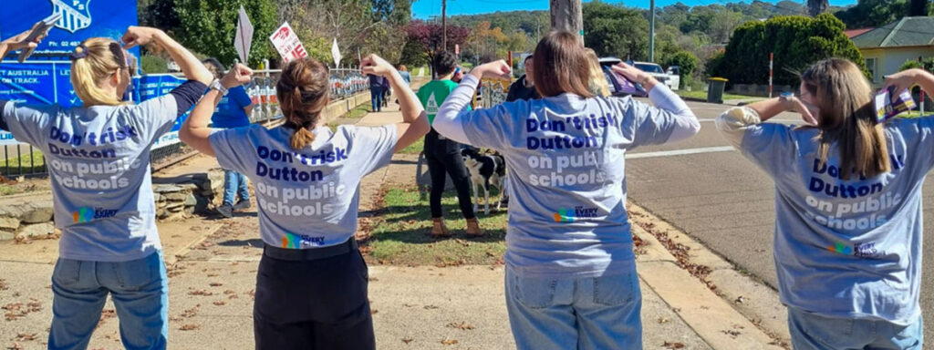 Four teachers wearing "Don't risk Dutton on public schools" t-shirts