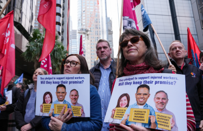 Two women hold placards opposing NSW Treasurer Daniel Mookhey’s proposed changes to workers compensation during a rally in Sydney.